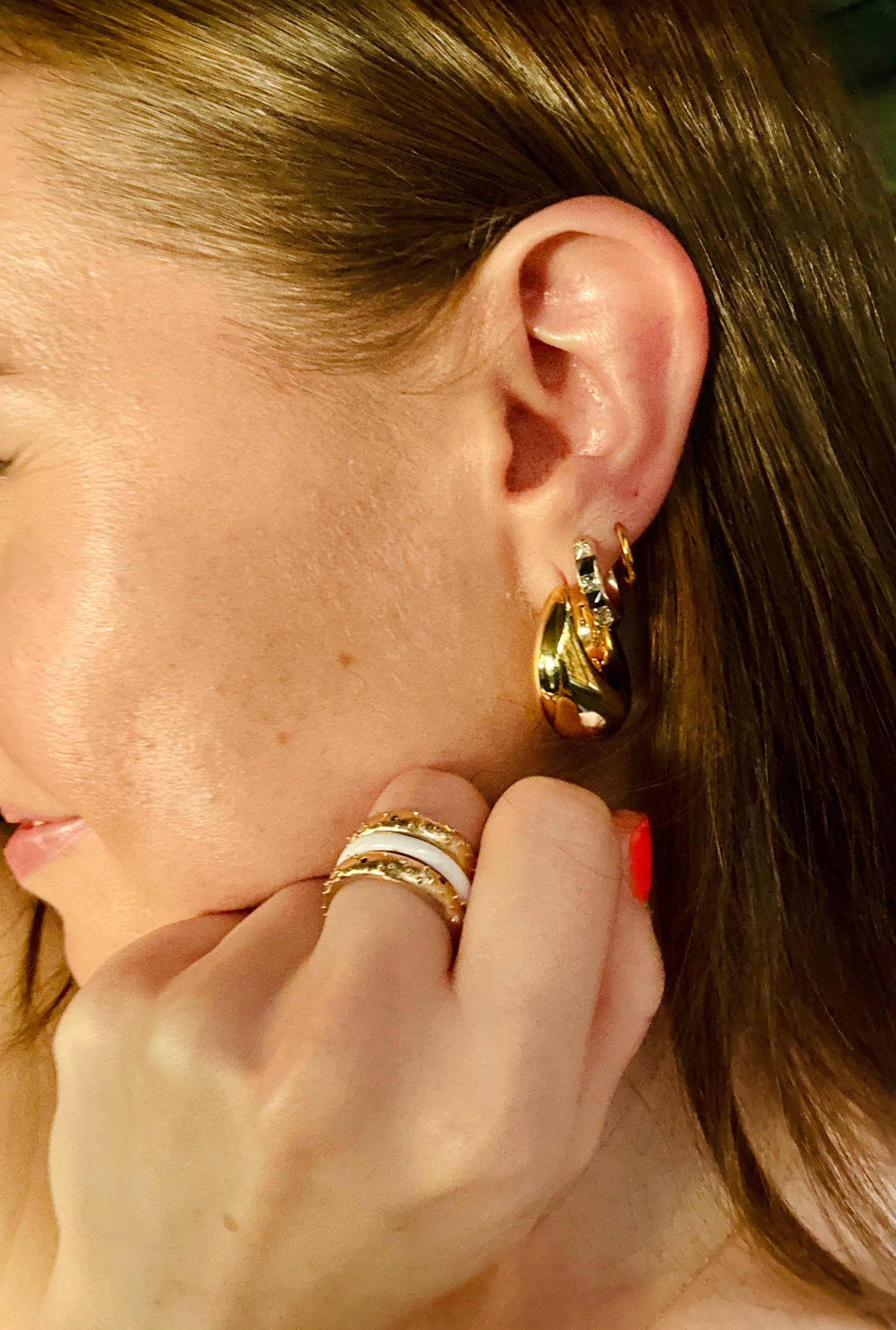 Elegant woman showcasing luxurious fine jewelry from Always, A., featuring dazzling gold earrings and a unique, eye-catching bagel-themed ring, blending sophistication with a touch of whimsy